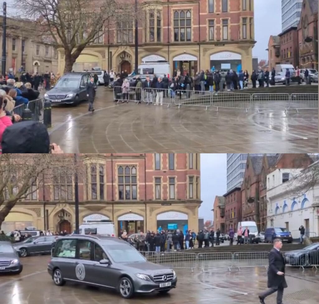 Photo of a hearse driving through the street with people either side watching