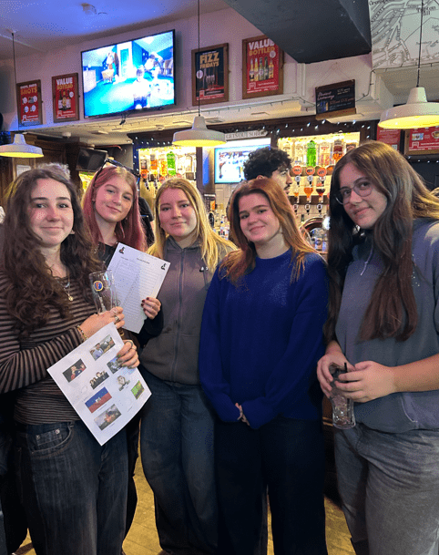 Group of people at stood up, holding answer sheets at a pub quiz
