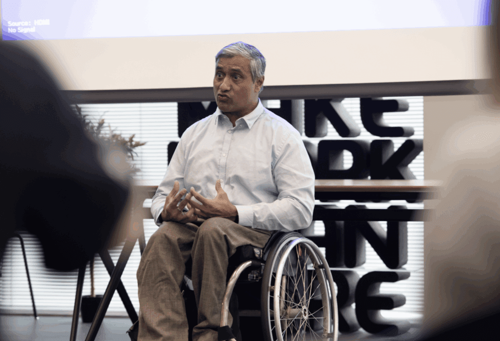 Man wearing blue dress shirt, sitting in wheelchair and speaking to group of peopl