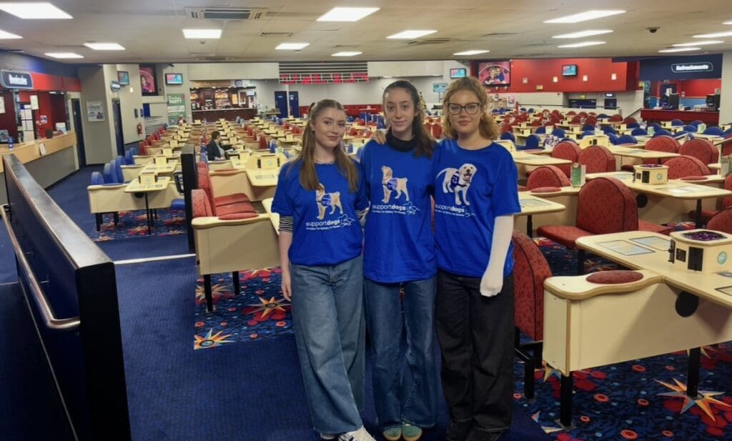 Support Dogs campaign team stand smiling in front of Mecca Bingo Hall in blue charity tops