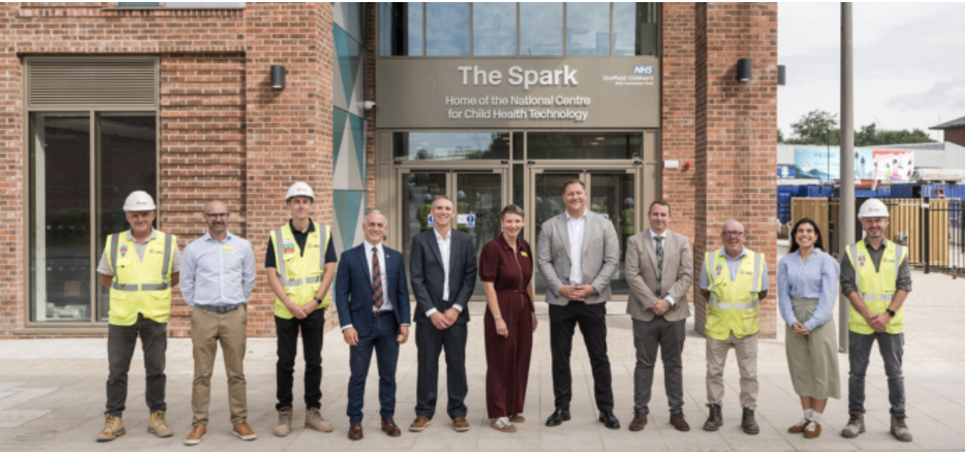 The Spark A line of eleven people, four of which in hi-vis and helmets, the other in suits and formal wear, stand outside a brick building with the name 'The Spark' written on the exterior.