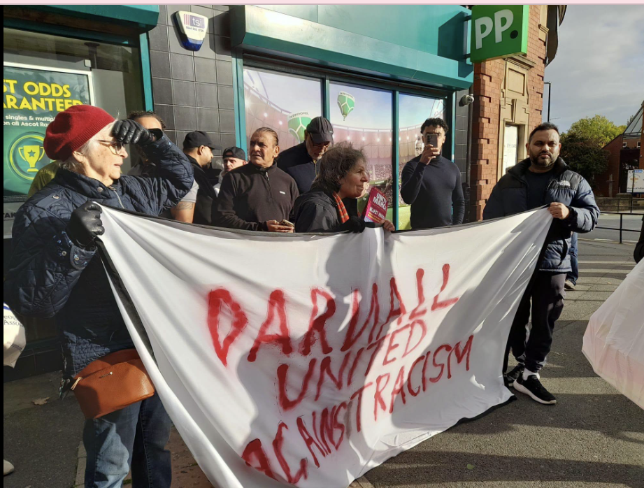 Screenshot 2026-10-24 at 09.22.48 A group of people holding up a banner that says 'DARNALL UNITED AGAINST RACISM'