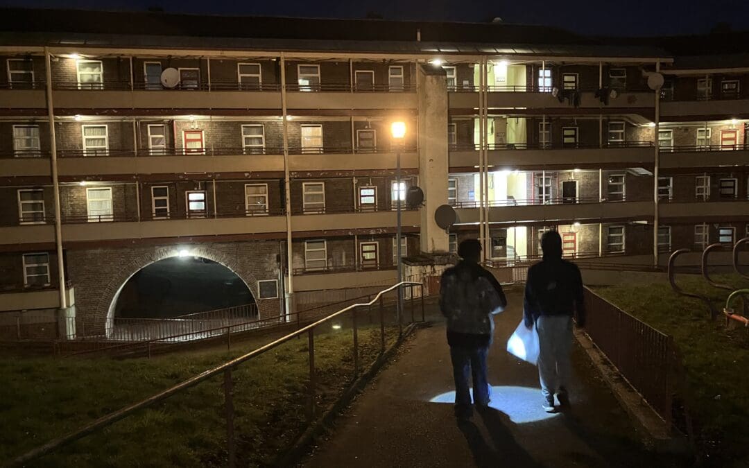 Two racers navigate through a park at night with a flashlight.