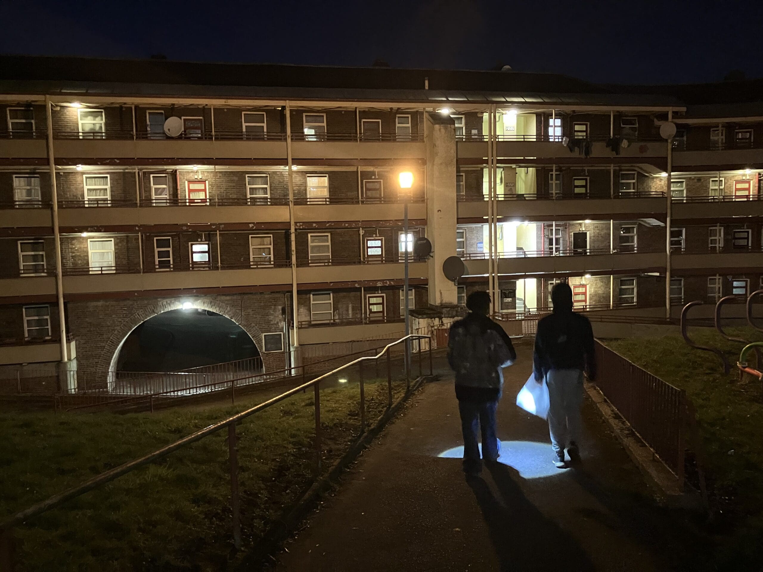 Two racers navigate through a park at night with a flashlight.